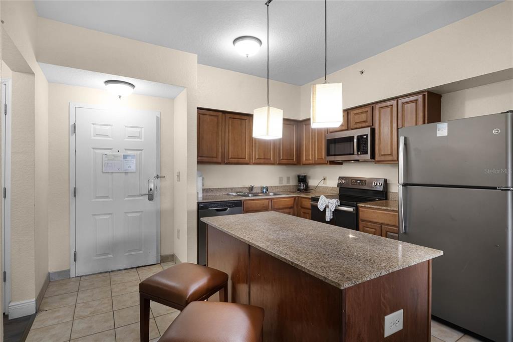 A kitchen with wood cabinets, granite countertops, a center island, and stainless steel appliances — 12527 FLORIDAYS RESORT DRIVE UNIT 512E, ORLANDO, FL