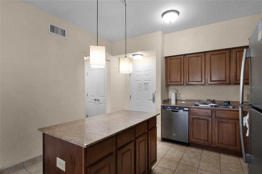 A kitchen features a granite-topped island, wooden cabinets, stainless steel appliances, and tile flooring — 12527 FLORIDAYS RESORT DRIVE UNIT 512E, ORLANDO, FL
