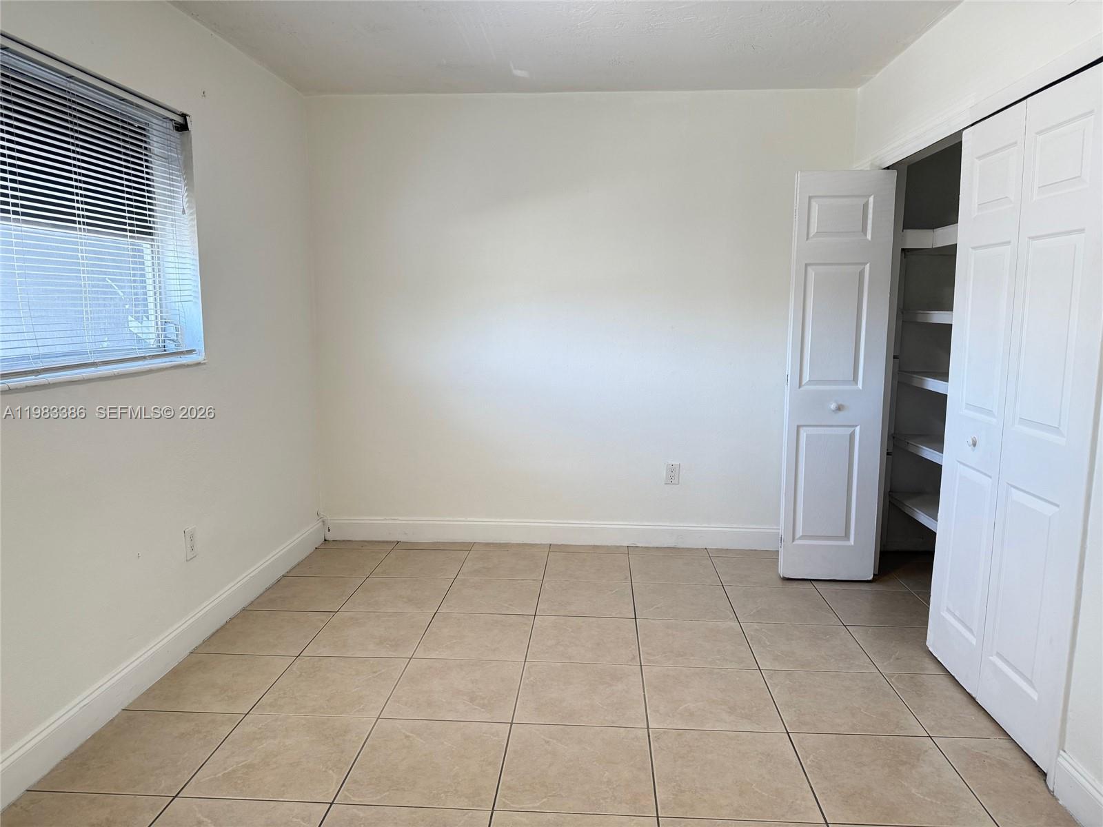 An empty room features beige tile flooring, white walls, a window with blinds, and a closet — 4300 SW 67th Ave # 38, Miami FL 33155, MIAMI, FL