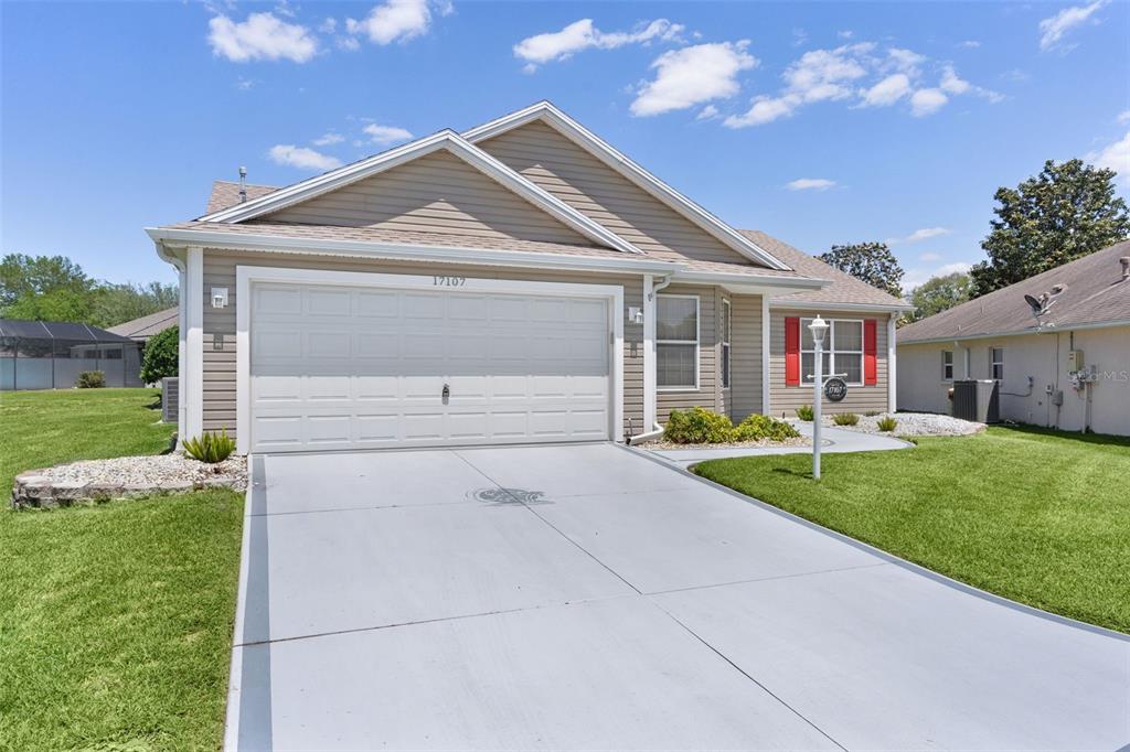 A single-story house with tan siding, a two-car garage, and a concrete driveway — 17107 SE 93RD EXETER COURT, THE VILLAGES, FL