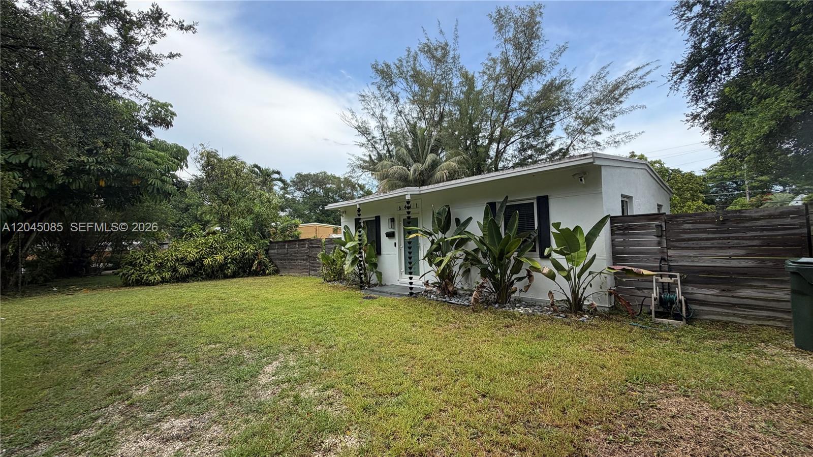 A white single-story house with a large lawn and tropical landscaping sits behind a fence — 6411 SW 62nd Ct, South Miami FL 33143, SOUTH MIAMI, FL