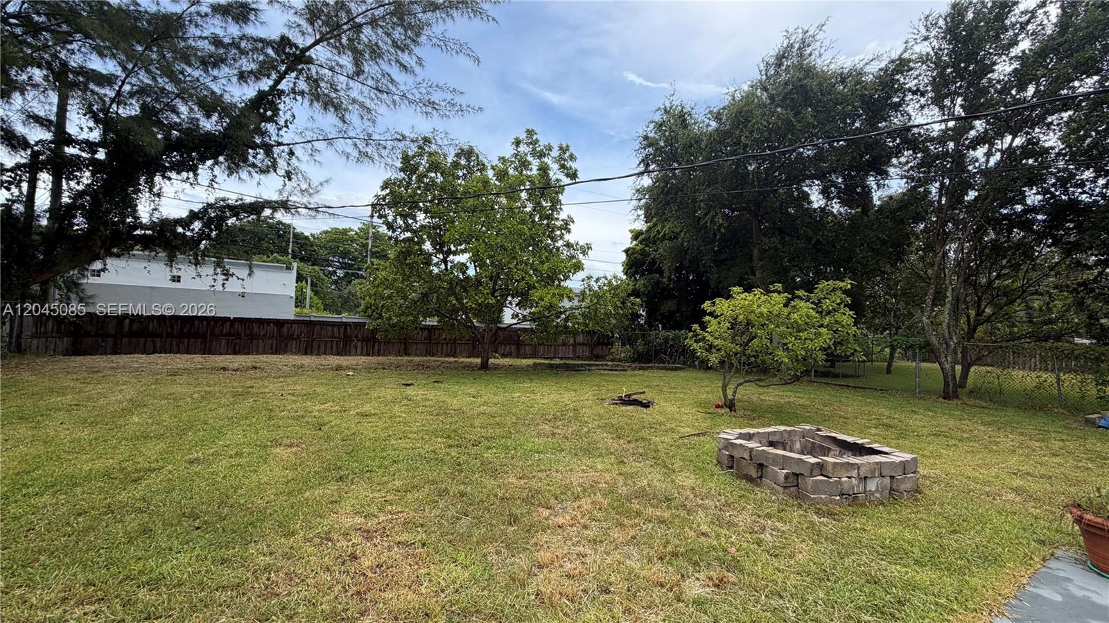 A grassy backyard features a stone fire pit, mature trees, and a wooden fence — 6411 SW 62nd Ct, South Miami FL 33143, SOUTH MIAMI, FL