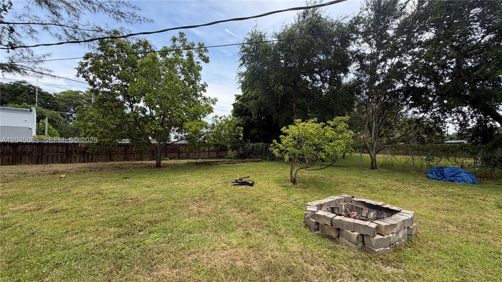 A grassy backyard features a stone fire pit, several trees, and a wooden fence — 6411 SW 62nd Ct, South Miami FL 33143, SOUTH MIAMI, FL