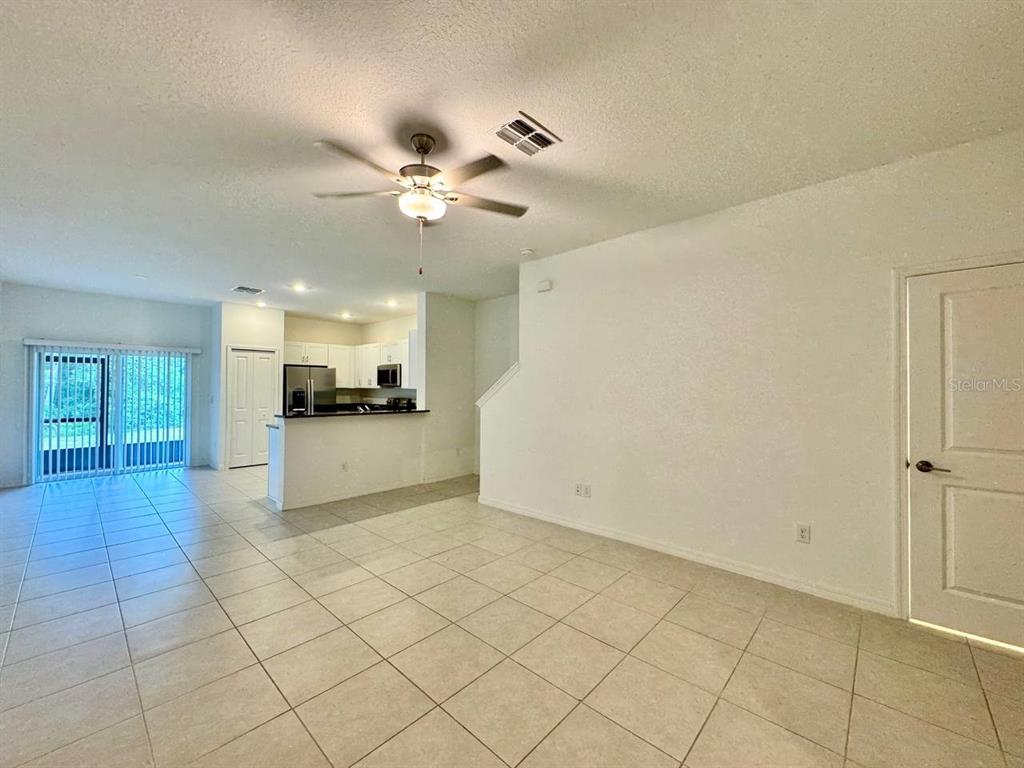 An open-concept living area with tile floors, a ceiling fan, and an adjacent kitchen — 17657 NECTAR FLUME DRIVE, LAND O LAKES, FL