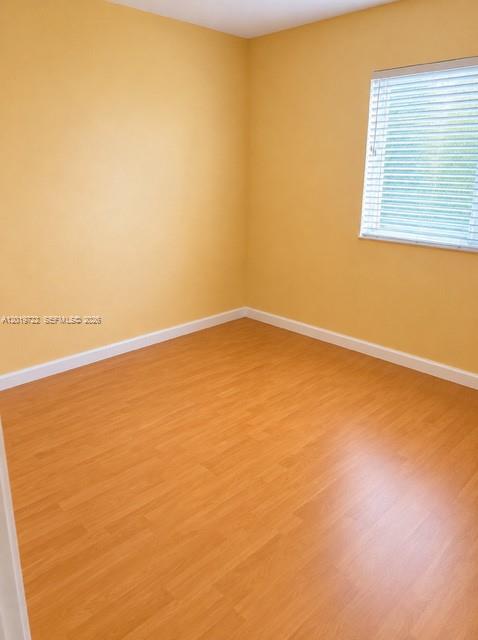 An empty bedroom features yellow walls, light wood-look flooring, and a window with white blinds — 14803 SW 9th Ln # 0, Miami FL 33194, MIAMI, FL