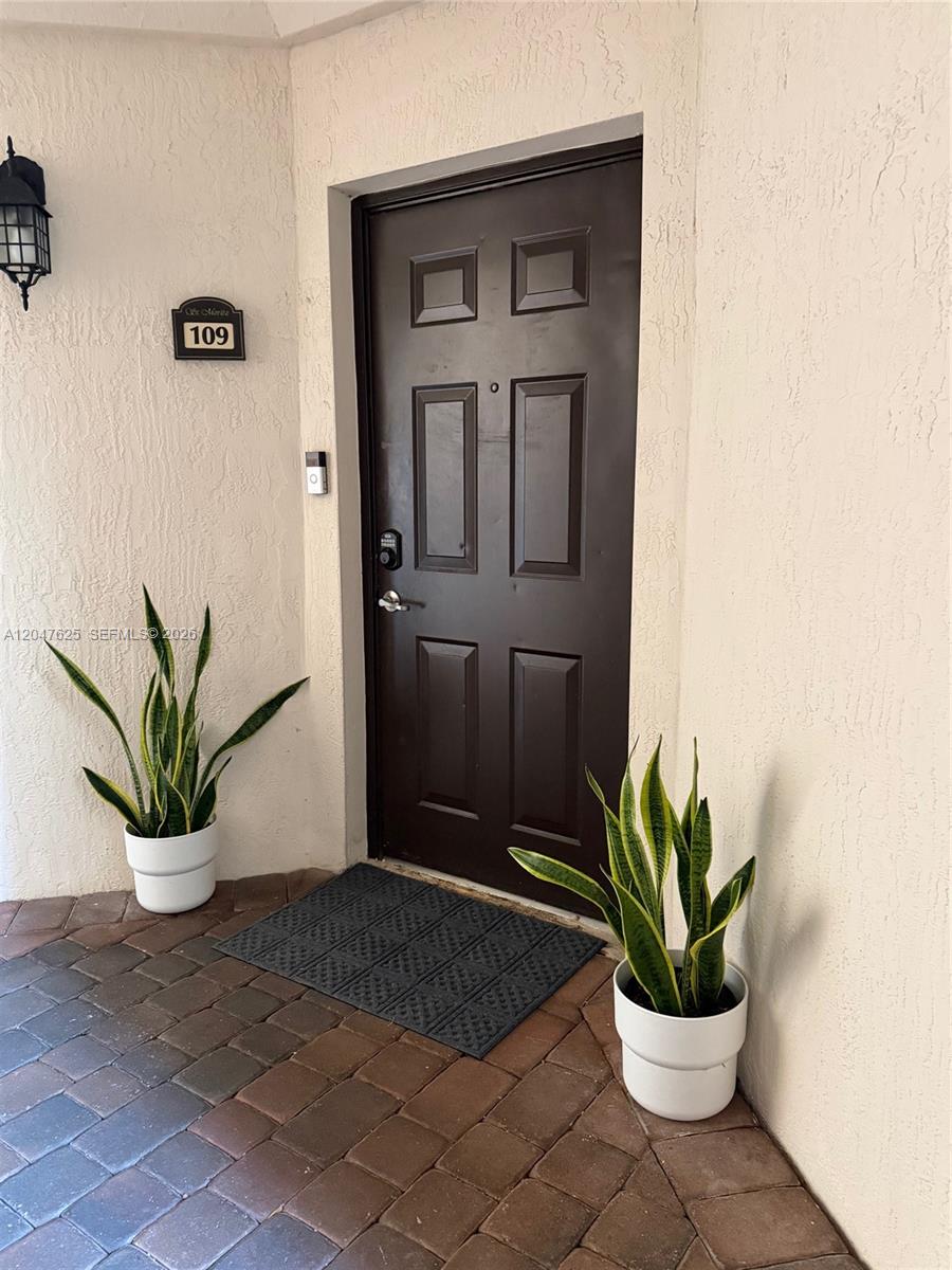A dark brown front door with a keypad lock sits between two potted snake plants — DORAL, FL