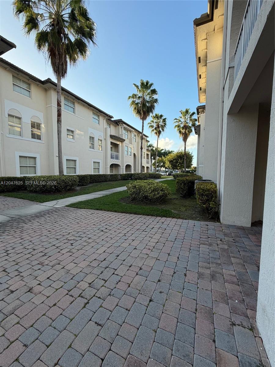 A paved walkway leads between two multi-story apartment buildings surrounded by palm trees and landscaping — DORAL, FL