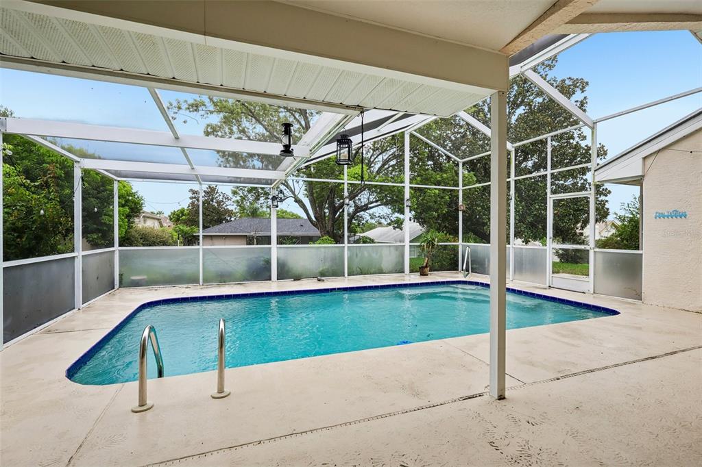 A screened-in patio features a rectangular swimming pool with a metal ladder and concrete deck — 1260 MASADA LANE, SPRING HILL, FL