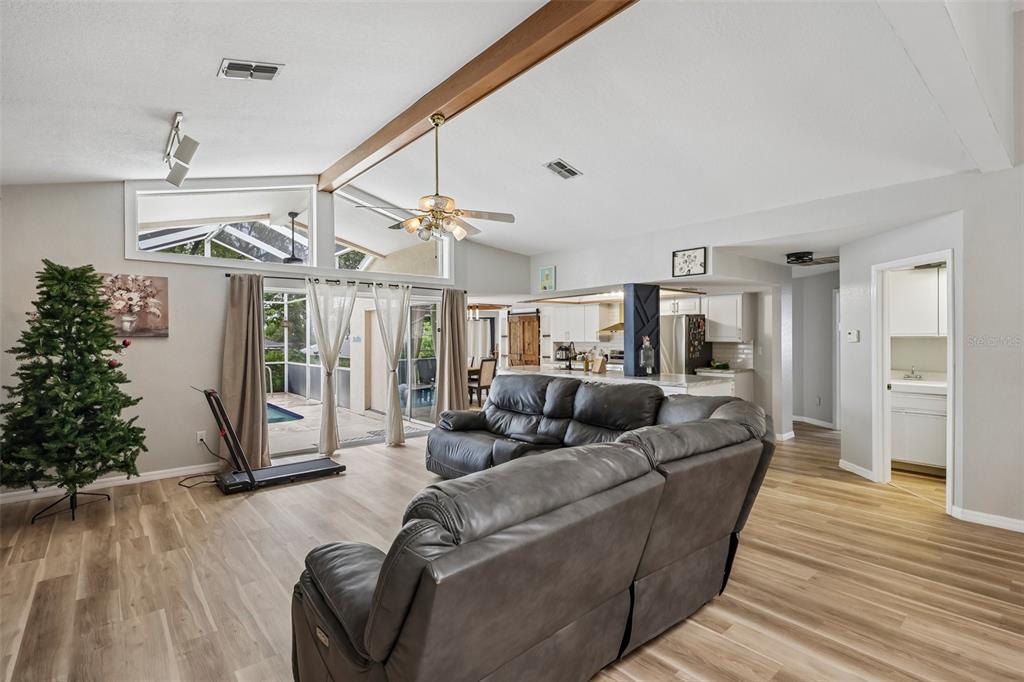 A living room with wood-look flooring, a vaulted ceiling, a ceiling fan, and a sliding door — 1260 MASADA LANE, SPRING HILL, FL