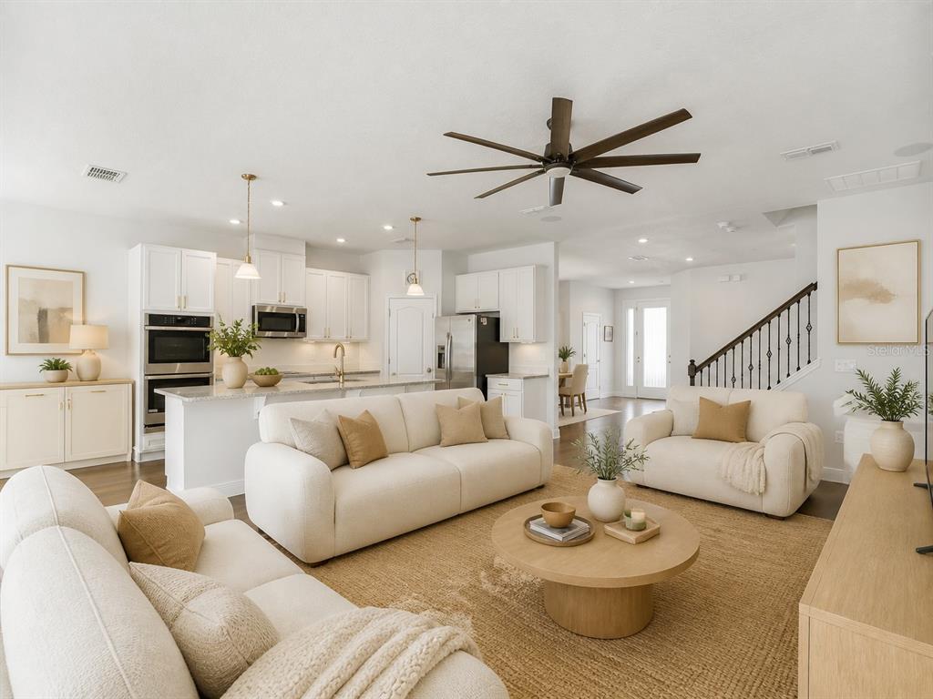 A bright open-concept living room features white sofas, a round coffee table, and a kitchen — 536 AFFIRMED WAY, DAVENPORT, FL