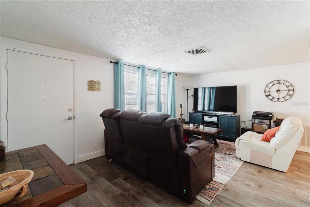 A living room features a dark brown reclining sofa, a white armchair, and wood flooring — 9803 RICHWOOD LANE, PORT RICHEY, FL