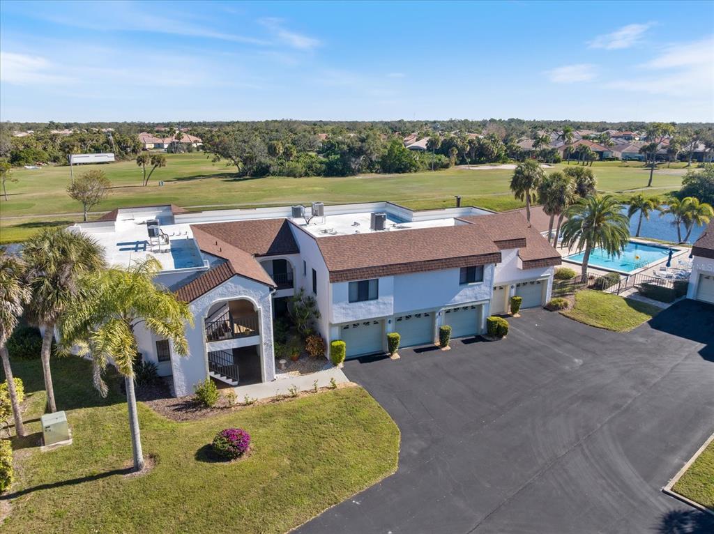 An aerial view shows a multi-unit residential building with a pool and golf course views — 822 CAPRI ISLES BOULEVARD UNIT 107, VENICE, FL