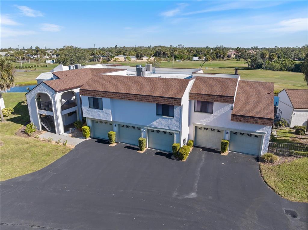 An aerial view of a multi-unit residential building with five garage doors and brown shingles — 822 CAPRI ISLES BOULEVARD UNIT 107, VENICE, FL