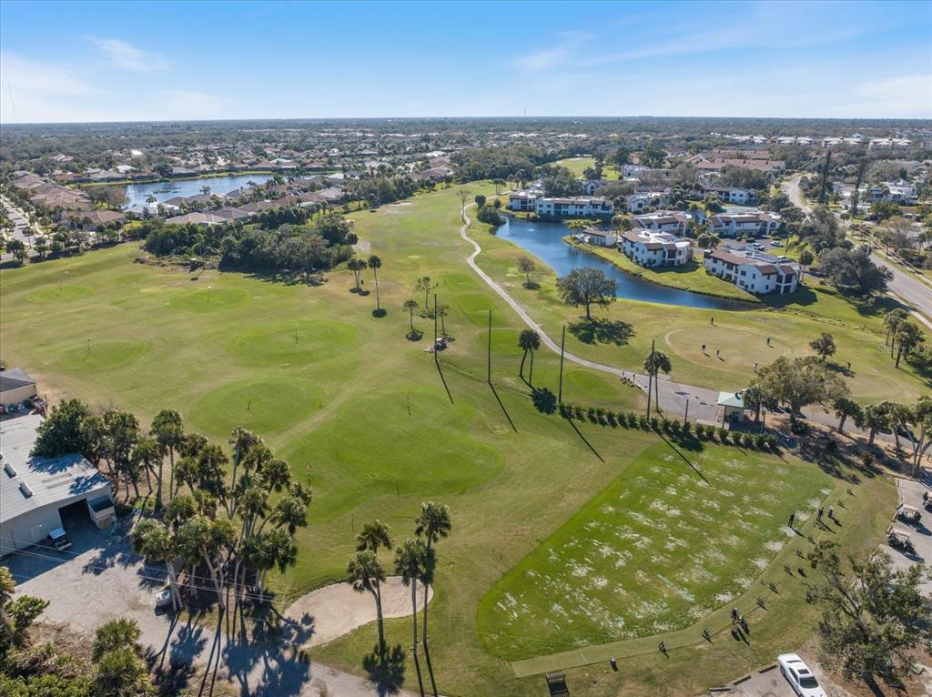 An aerial view of a golf course with a driving range, putting greens, and nearby buildings — 822 CAPRI ISLES BOULEVARD UNIT 107, VENICE, FL