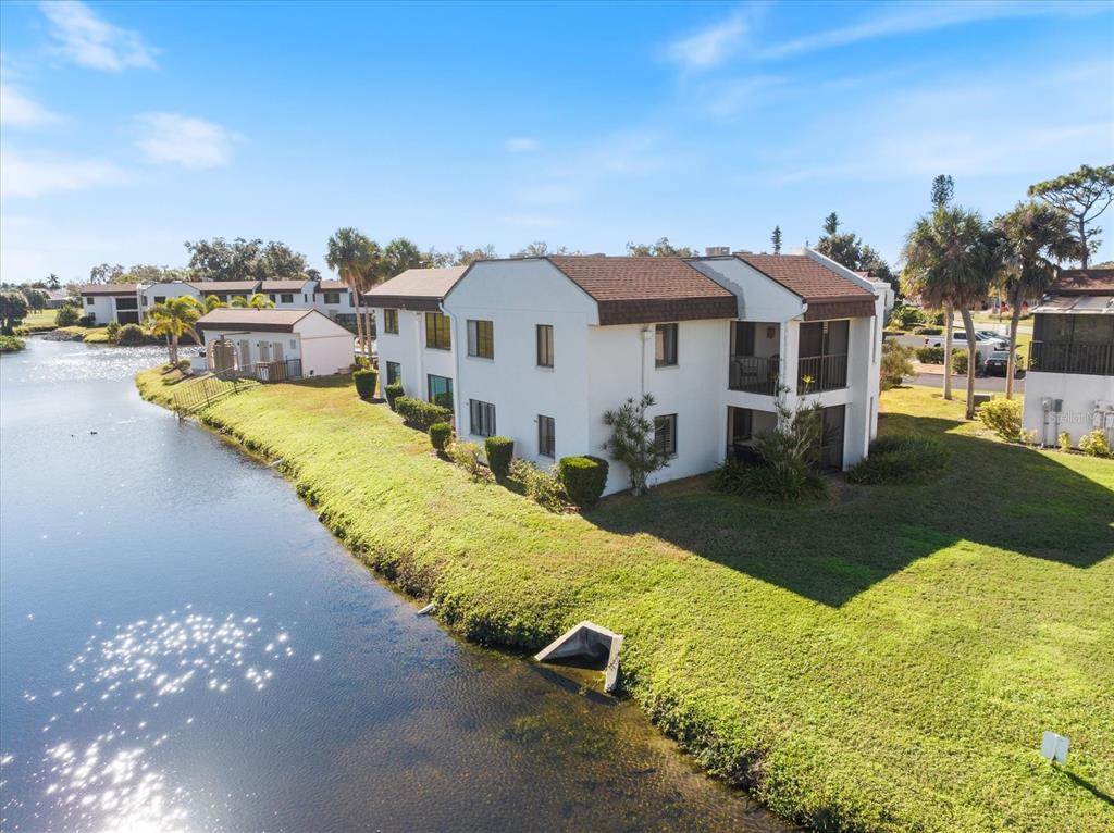 An aerial view of a two-story apartment building situated next to a small lake — 822 CAPRI ISLES BOULEVARD UNIT 107, VENICE, FL