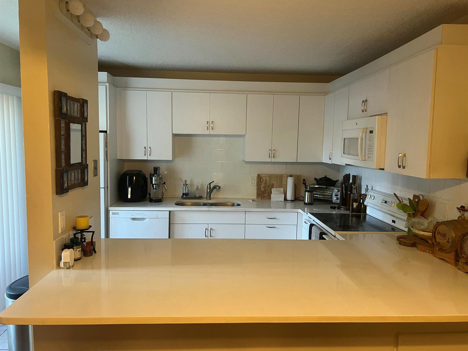 A kitchen with white cabinets, white countertops, and a breakfast bar overlooking the sink area — 825 Center Street # 3c, Jupiter FL 33458, JUPITER, FL