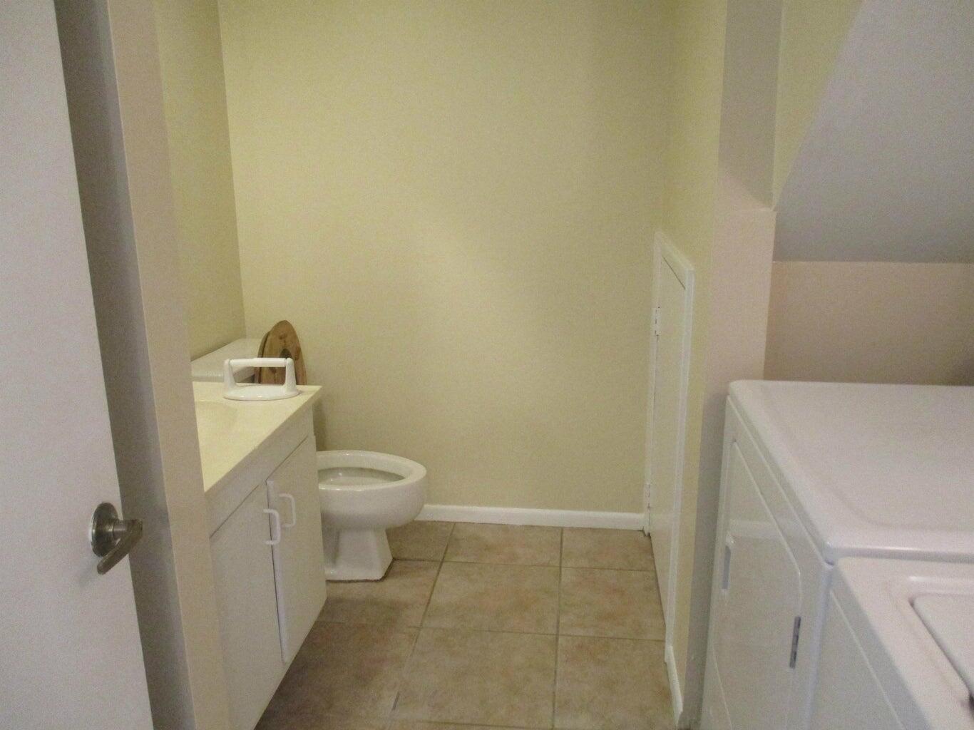 A small bathroom features a white vanity, a toilet, and tile flooring next to laundry appliances — 825 Center Street # 3c, Jupiter FL 33458, JUPITER, FL