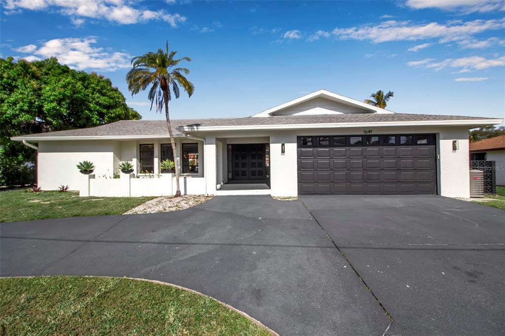 A single-story house with a white exterior, a dark garage door, and a palm tree — 1649 STANFORD LANE, SARASOTA, FL
