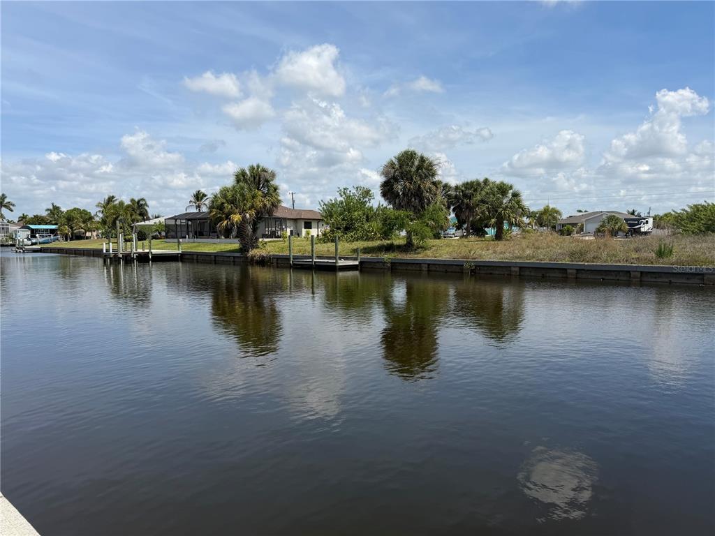 A canal view shows a grassy waterfront lot with palm trees and a boat dock — 17122 MARYDALE ROAD, PORT CHARLOTTE, FL