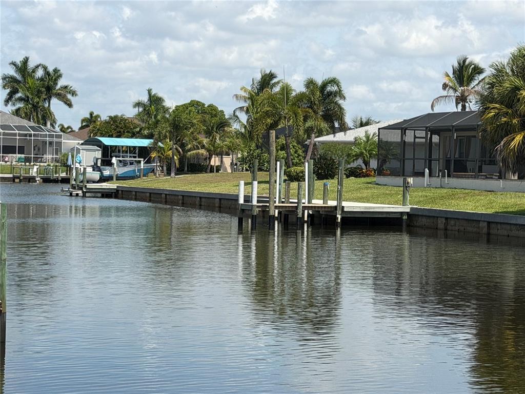 A canal view showing a wooden dock, boat lift, and houses with screened-in lanais — 17122 MARYDALE ROAD, PORT CHARLOTTE, FL