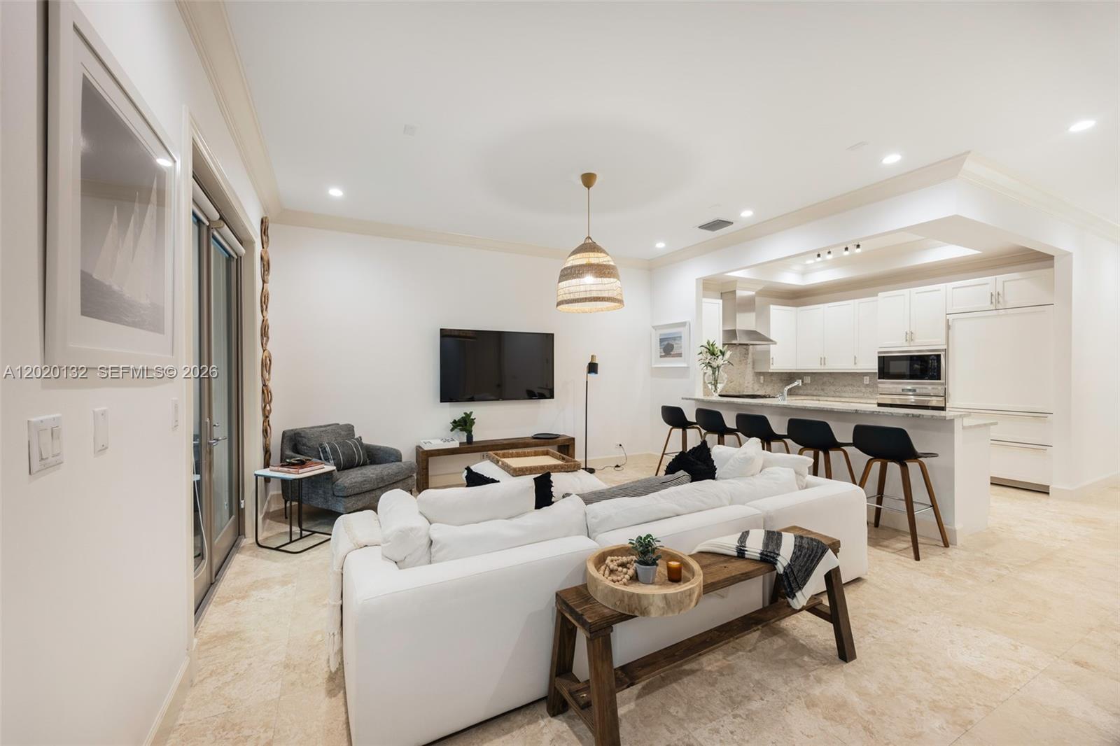 A bright, open-concept living room features a white sectional sofa, kitchen island, and tile flooring — 7430 SW 56th Ct, Miami FL 33143, MIAMI, FL