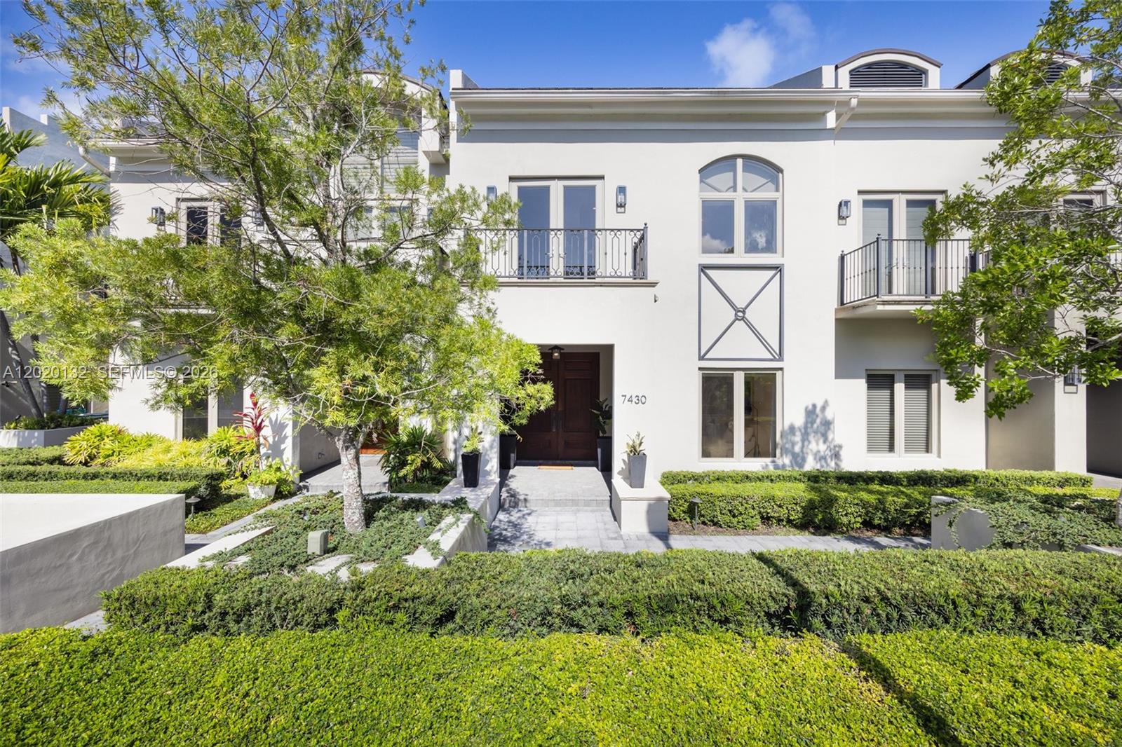 A two-story white stucco townhouse features a front entrance, balconies, and manicured landscaping — 7430 SW 56th Ct, Miami FL 33143, MIAMI, FL