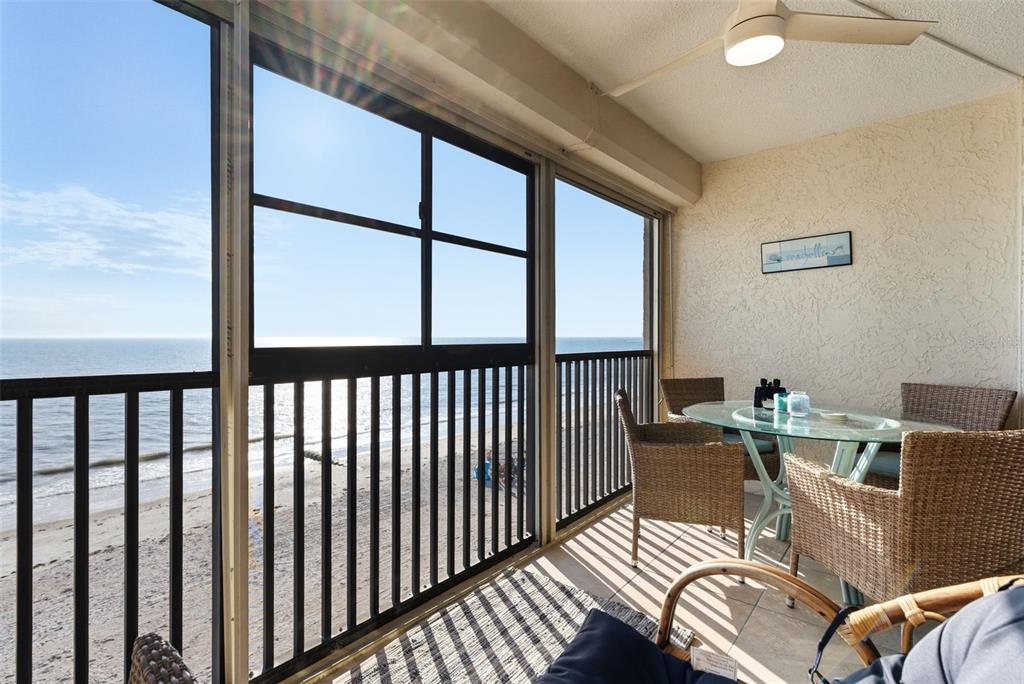 A balcony with a glass-topped table and wicker chairs overlooks a beach and ocean — 15462 GULF BOULEVARD UNIT 406, ST PETERSBURG, FL