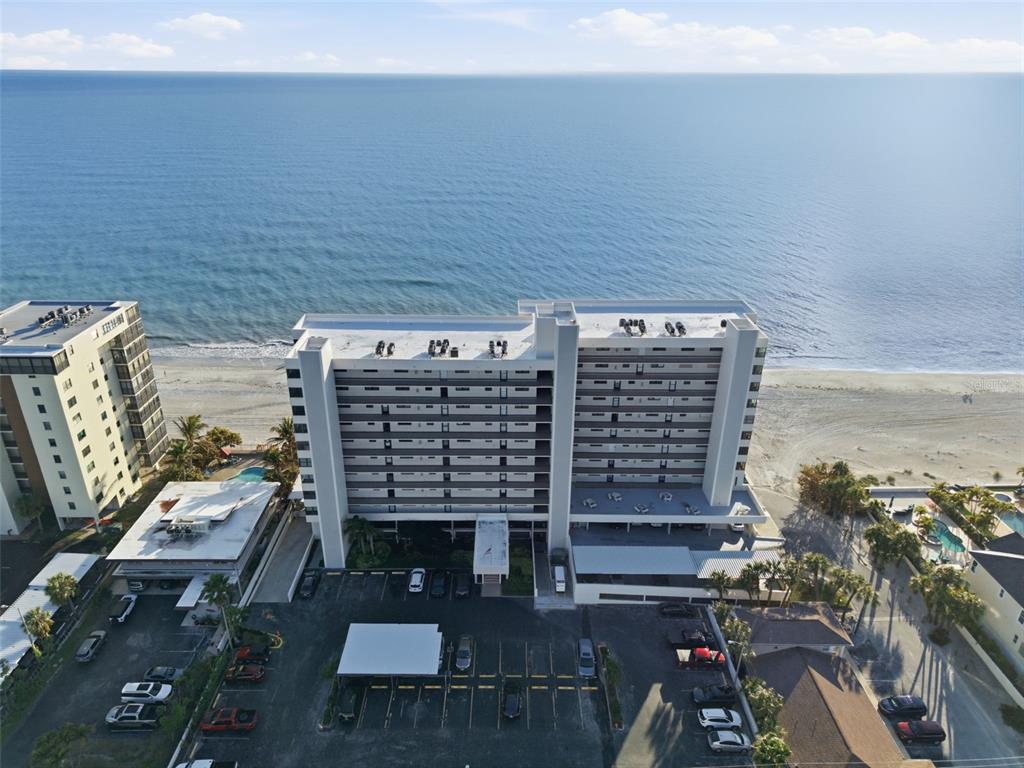 An aerial view shows a multi-story beachfront condominium building with a parking lot in front — 15462 GULF BOULEVARD UNIT 406, ST PETERSBURG, FL