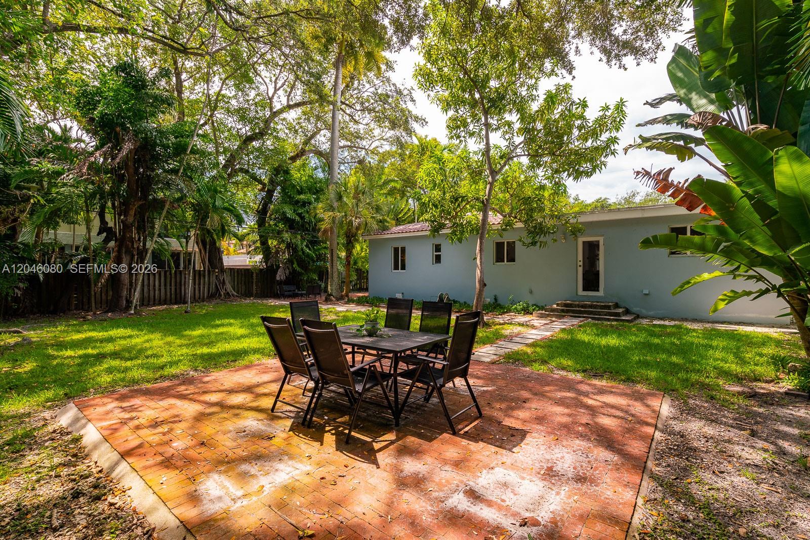 A brick patio with a dining set sits in a backyard behind a light blue house — 2215 Tequesta Ln, Miami FL 33133, MIAMI, FL
