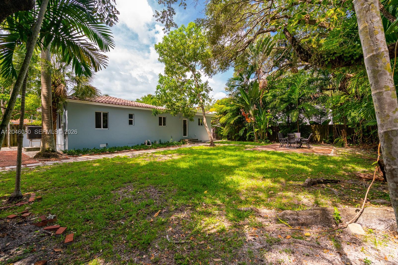 A backyard with a light blue house, a brick patio, and mature trees — 2215 Tequesta Ln, Miami FL 33133, MIAMI, FL