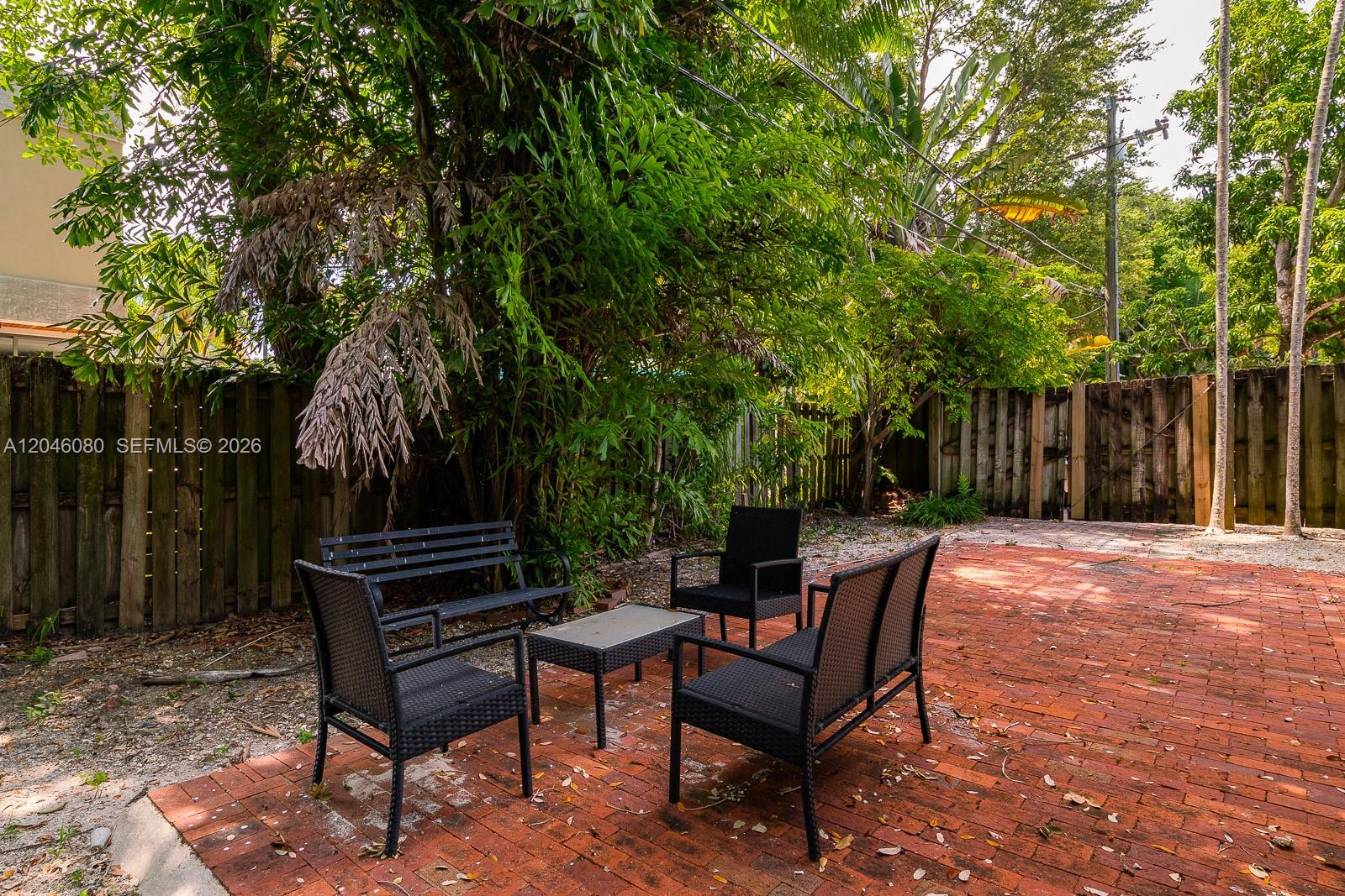 A brick patio features outdoor furniture set against a wooden fence and lush trees — 2215 Tequesta Ln, Miami FL 33133, MIAMI, FL