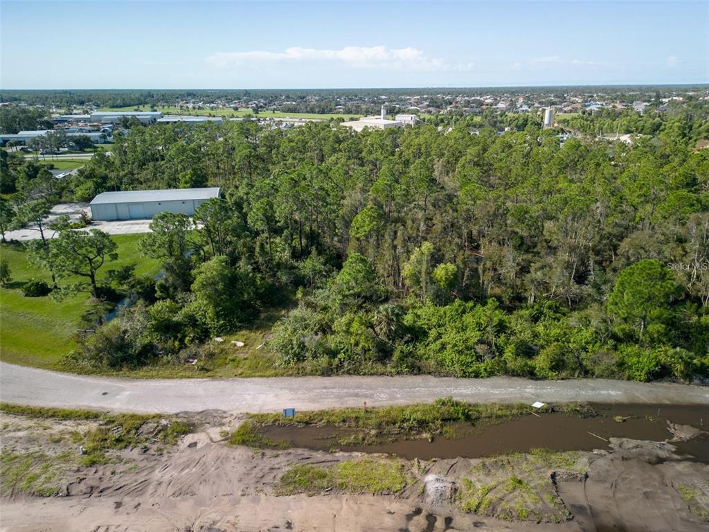 An aerial view shows a wooded lot adjacent to a paved road and industrial buildings — 10271 PHEASANT BOULEVARD, PUNTA GORDA, FL