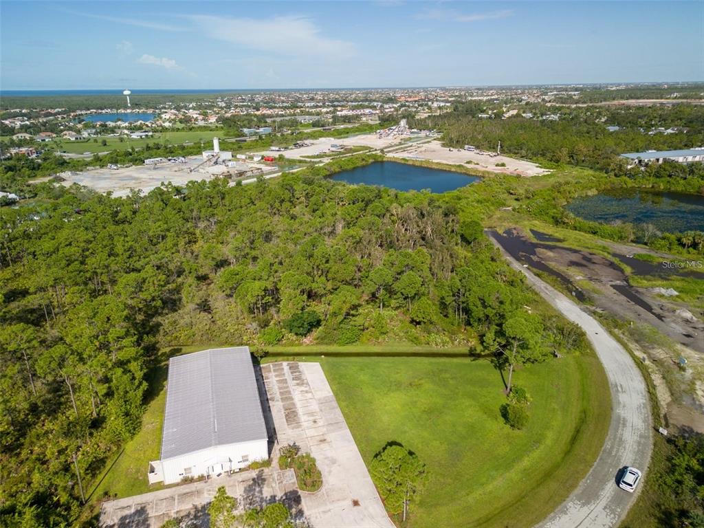 An aerial view shows a warehouse building with a concrete parking lot near wooded areas — 10271 PHEASANT BOULEVARD, PUNTA GORDA, FL
