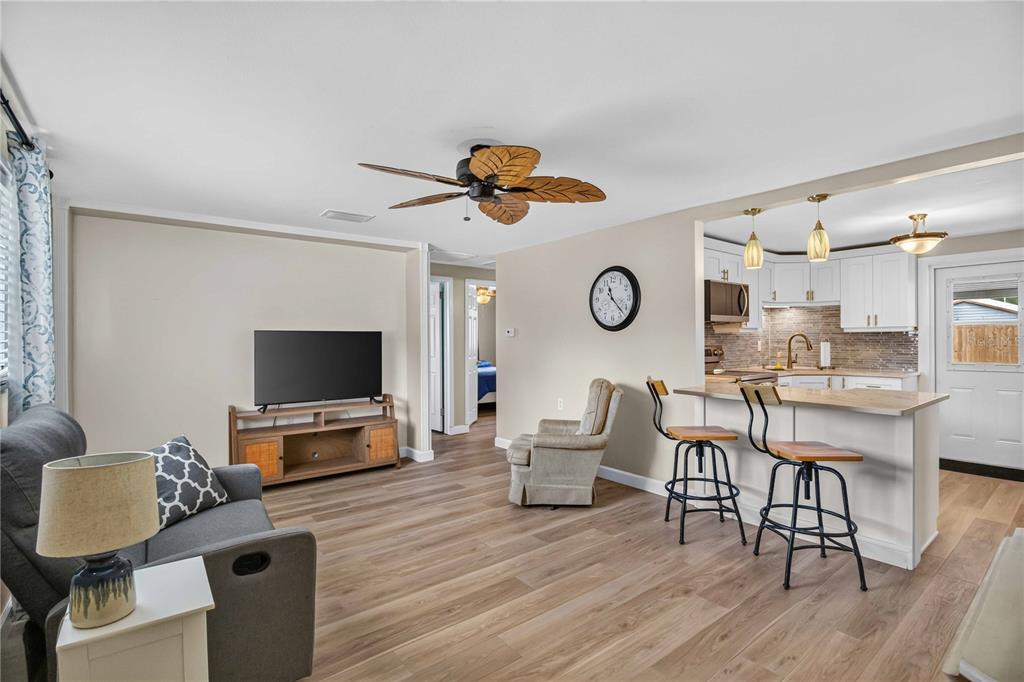 A living room with wood-look flooring flows into an open kitchen with a breakfast bar — 4620 3RD AVENUE W, PALMETTO, FL