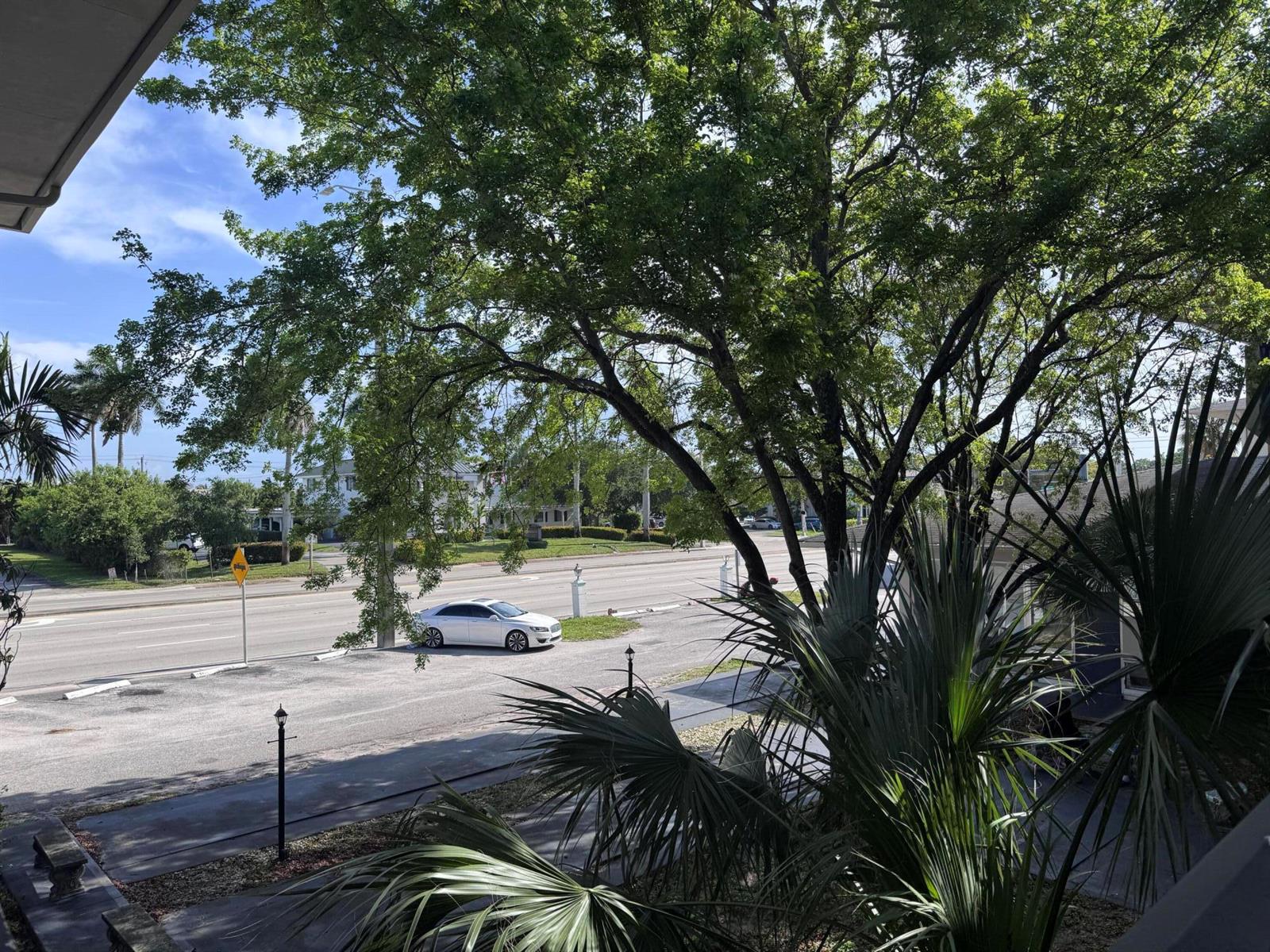 A view from an elevated balcony overlooking a street, a parked white car, and trees — 1150 E Sample Road # 204, Pompano Beach FL 33064, POMPANO BEACH, FL