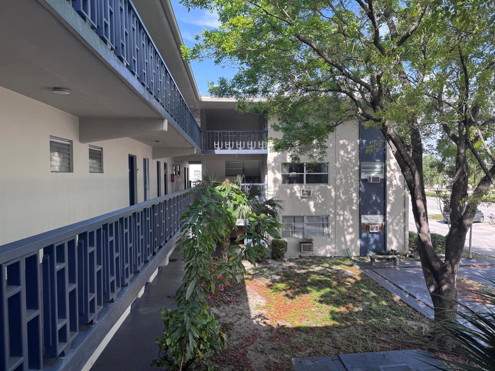 An exterior view of a multi-story apartment building with open-air walkways and a central courtyard — 1150 E Sample Road # 204, Pompano Beach FL 33064, POMPANO BEACH, FL