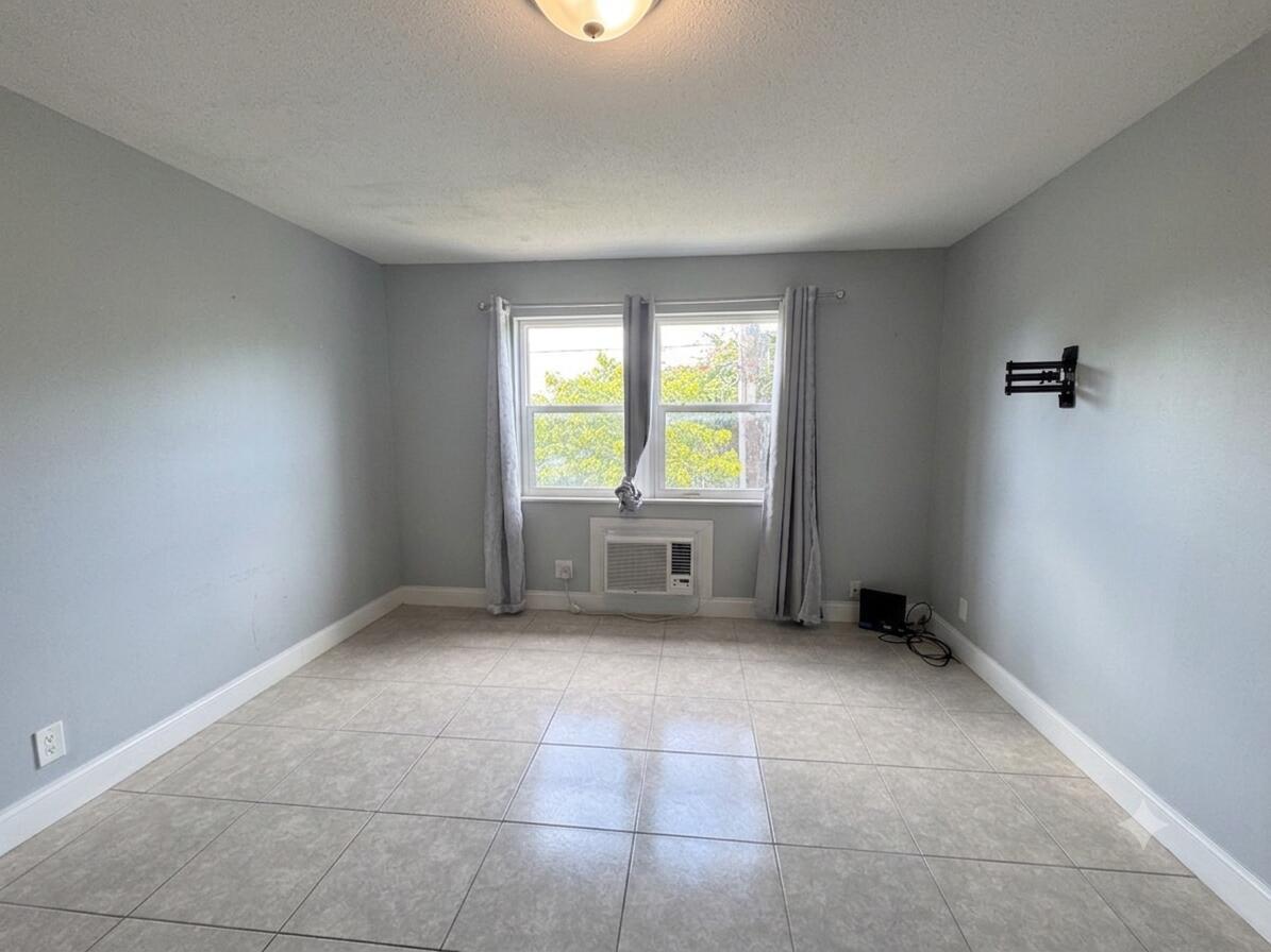 An empty room with light gray walls, tile flooring, a window, and a wall-mounted AC unit — 1150 E Sample Road # 204, Pompano Beach FL 33064, POMPANO BEACH, FL
