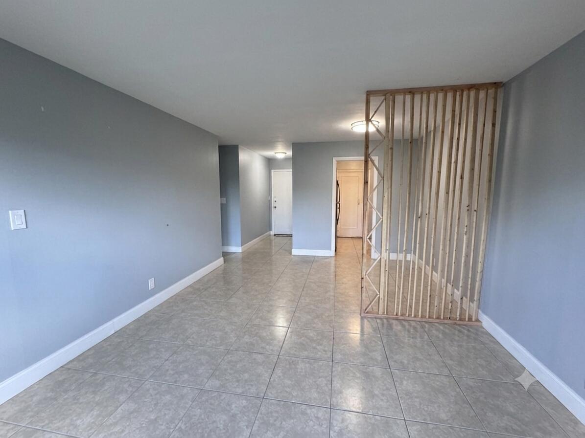 An empty room with gray walls, tile flooring, and a decorative wooden slat room divider — 1150 E Sample Road # 204, Pompano Beach FL 33064, POMPANO BEACH, FL
