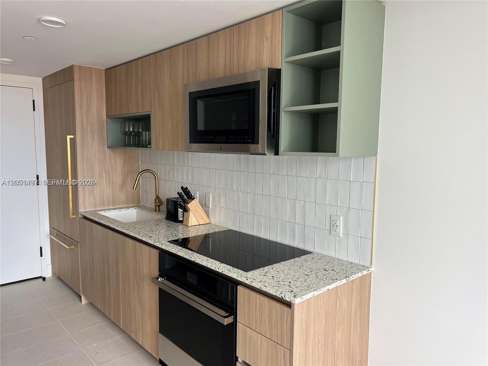 A modern kitchen features wood-grain cabinets, light terrazzo countertops, and a sage green open shelf — 159 NE 6th St # 2807, Miami FL 33132, MIAMI, FL