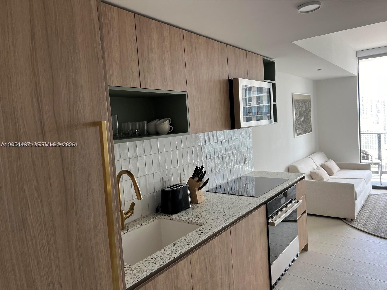 A modern kitchen features wood-grain cabinets, a terrazzo countertop, and a white tiled backsplash — 159 NE 6th St # 2807, Miami FL 33132, MIAMI, FL