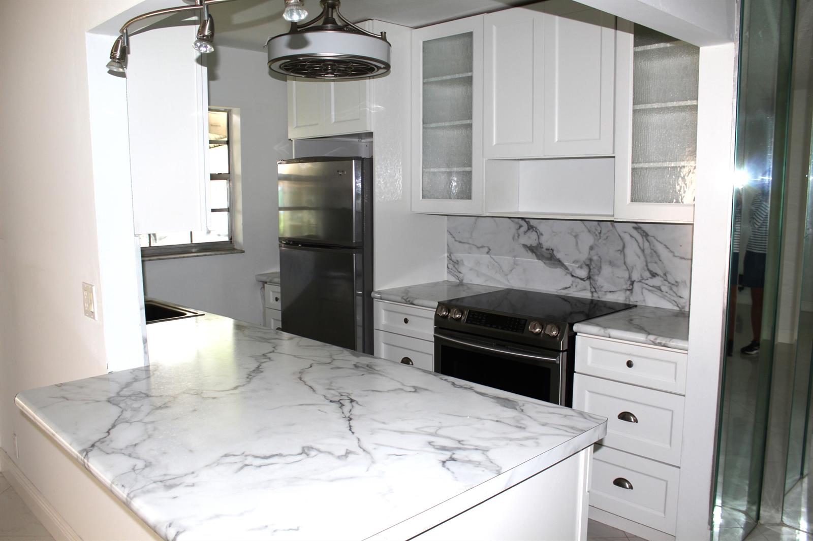 A kitchen features white cabinets, marble-patterned countertops, stainless steel appliances, and a central island — 4755 NW 3rd Court # C, Delray Beach FL 33445, DELRAY BEACH, FL