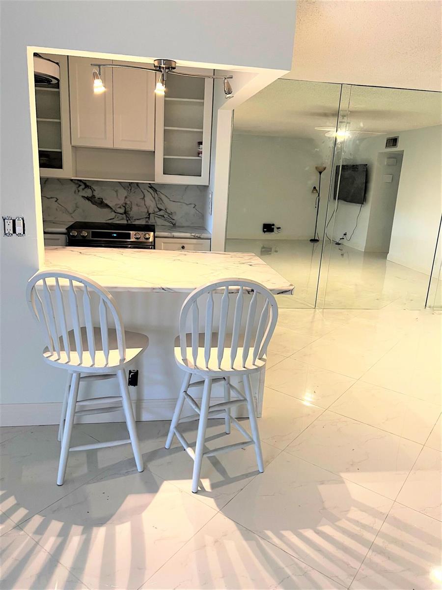 A kitchen with a marble-topped breakfast bar and two white chairs faces a mirrored room — 4755 NW 3rd Court # C, Delray Beach FL 33445, DELRAY BEACH, FL