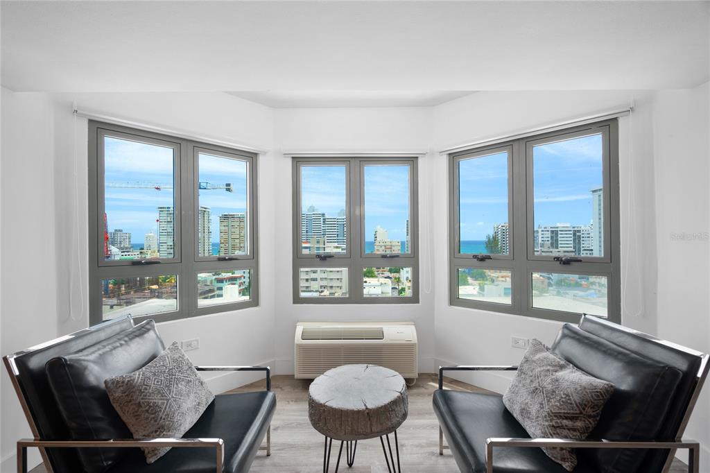 A living area with two black leather chairs, a wood-slice table, and large bay windows — 103 AVENIDA JOSE DE DIEGO UNIT 803N, SAN JUAN, PR