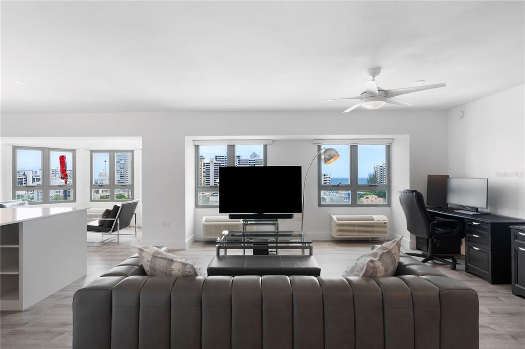 A living room features a grey tufted sofa, a television, and a desk near windows — 103 AVENIDA JOSE DE DIEGO UNIT 803N, SAN JUAN, PR
