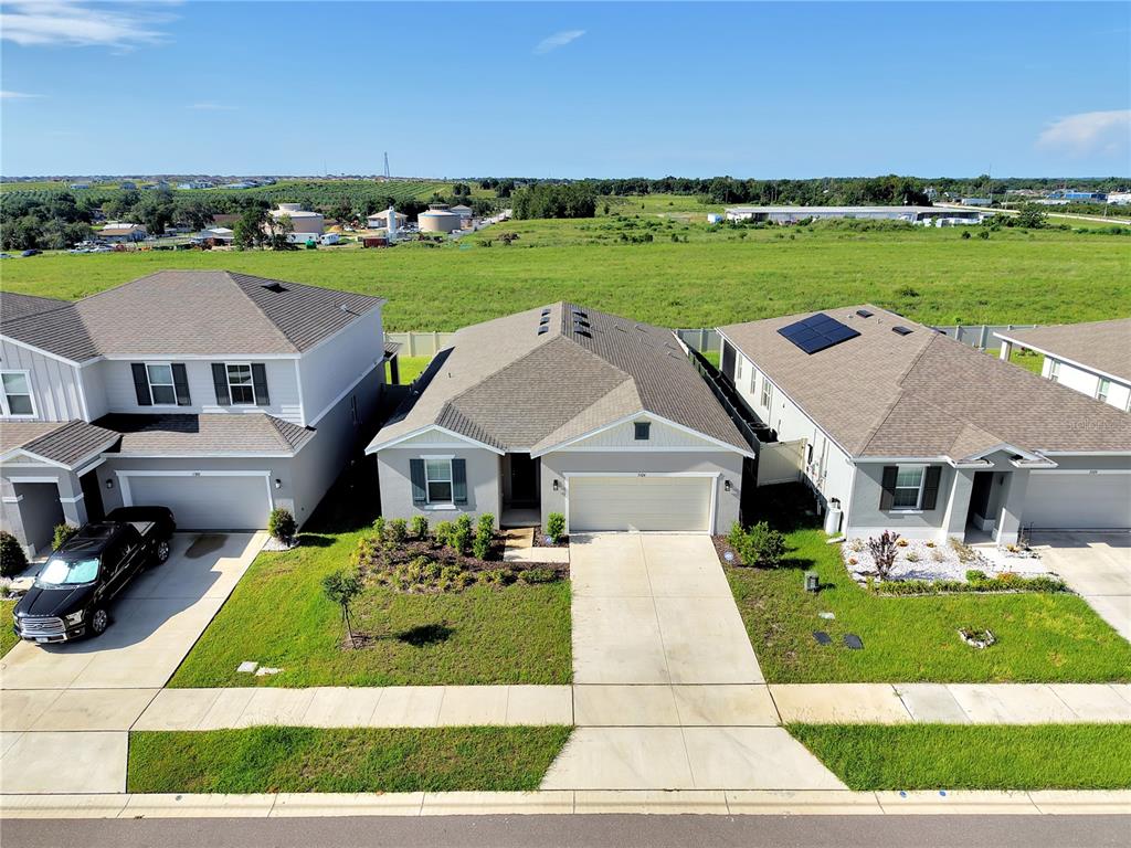 An aerial view shows three suburban houses with driveways and lawns facing a large field — 3324 CHICORY COURT, LAKE HAMILTON, FL