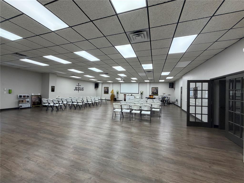 A large, open room with wood-look flooring, a drop ceiling, and rows of white chairs — 208 E LAKE AVENUE, AUBURNDALE, FL