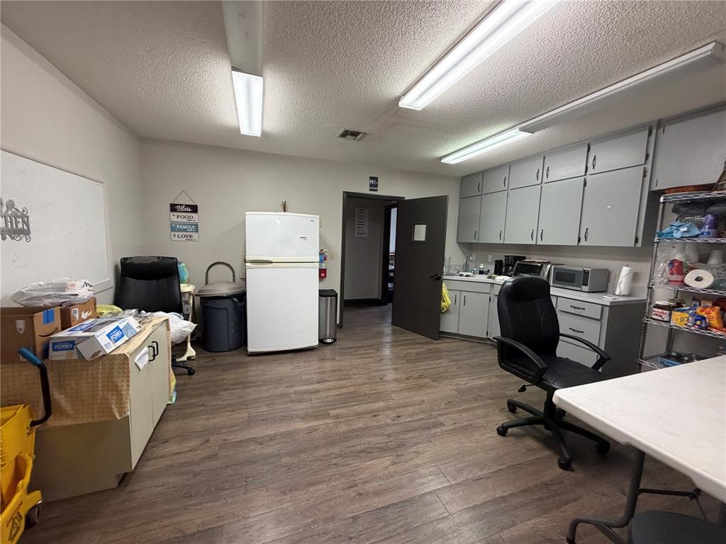 A breakroom features gray cabinets, a white refrigerator, two office chairs, and wood-look flooring — 208 E LAKE AVENUE, AUBURNDALE, FL