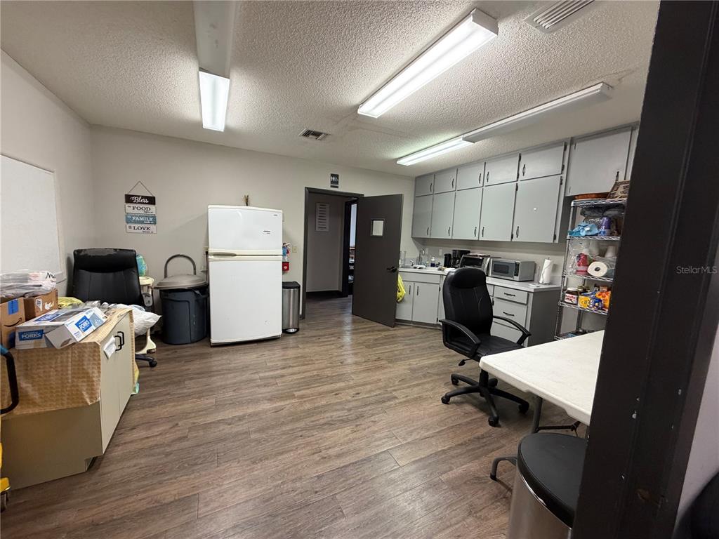 A breakroom features wood-look flooring, gray cabinetry, a white refrigerator, and office chairs — 208 E LAKE AVENUE, AUBURNDALE, FL