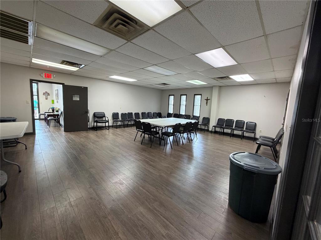 A large room with wood-look flooring, a drop ceiling, and several chairs arranged around tables — 208 E LAKE AVENUE, AUBURNDALE, FL