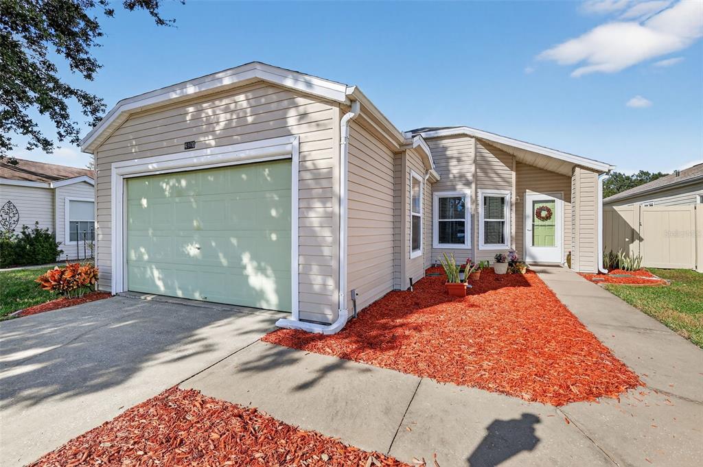 A tan, single-story house features a light green garage door and red mulch landscaping — 4900 HERON RUN CIRCLE, LEESBURG, FL